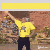a man in a yellow shirt is dancing in front of a wall with cartoon characters .