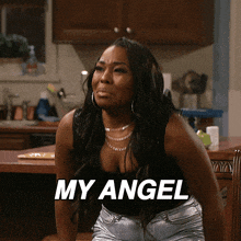 a woman is sitting in a kitchen with the words " my angel " on the screen