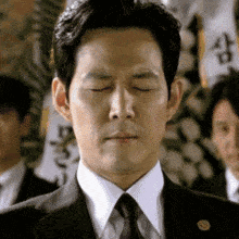 a man in a suit and tie with his eyes closed stands in front of a group of men