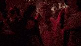 a group of people are dancing in a dark room with a red light