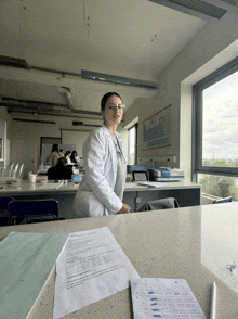 a woman in a lab coat stands in front of a table with papers on it