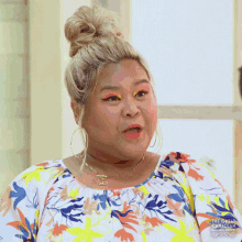 a woman with a bun on her head is wearing a floral shirt and earrings .