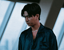 a man wearing a blue shirt and a silver necklace looks down