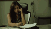 a woman sits at a desk talking on the phone
