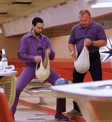 two men are playing bowling in a bowling alley and one is wearing purple pants
