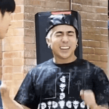 a man wearing a hat and a black shirt is standing in front of a brick wall and smiling .