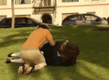 a man in an orange shirt is kneeling down next to another man laying on the grass