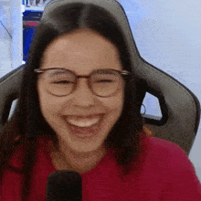 a girl wearing glasses and a red shirt is laughing in front of a microphone