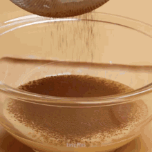 cocoa powder is being poured into a glass bowl which says easy plus on the bottom