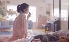 a woman is sitting on a bed with a teddy bear and a piano and the word x is on the bottom right corner