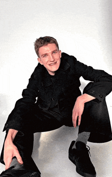 a man in a black jacket and black pants is sitting on the floor