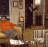 a man is sitting on a couch in a living room while a man in a suit stands in the doorway .