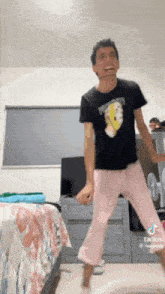 a man in a black shirt and pink pajamas is dancing in a bedroom .