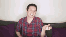 a young man in a plaid shirt is sitting on a couch with purple pillows