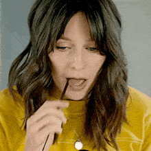 a woman in a yellow shirt is eating something with a straw