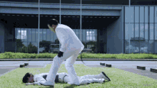 a man in a white suit helps another man laying on the grass