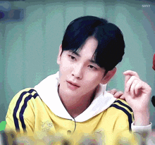 a young man wearing a yellow adidas sweatshirt looks at the camera