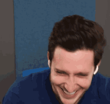 a man in a blue shirt is laughing with his eyes closed and wearing ear buds .
