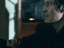 a man wearing glasses and a black shirt looks at something