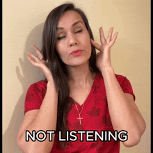 a woman in a red shirt covering her ears with her hands and the words " not listening " above her