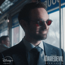 a man in a suit and tie is wearing sunglasses and a daredevil born again poster