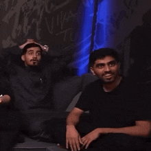 two men are sitting in front of a wall with the word viva on it