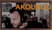 a man wearing headphones is sitting in front of a computer screen that says akoukou