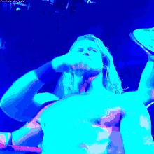 a wrestler is standing in a ring with a blue light shining on his chest .