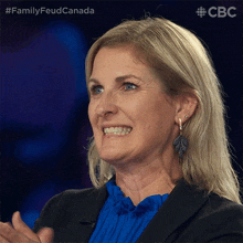 a woman in a blue shirt and black jacket is smiling and clapping with a cbc logo in the background