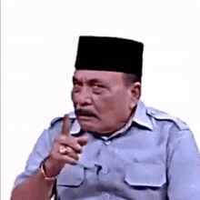 a man wearing a hat and a blue shirt is pointing his finger at something .