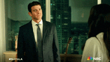a man in a suit and tie is standing next to a woman in a white shirt with the nbc logo on the bottom right