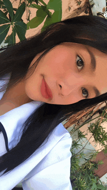 a girl with long black hair takes a selfie with a plant in the background