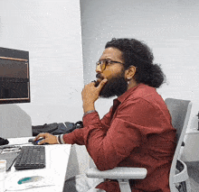a man in a red shirt sits in front of a computer monitor