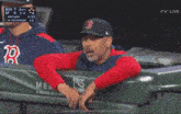 a man in a red sox hat is pointing at the scoreboard
