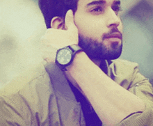 a man with a beard is wearing a watch and covering his ear