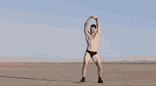a shirtless man in black underwear is standing on a sandy beach .
