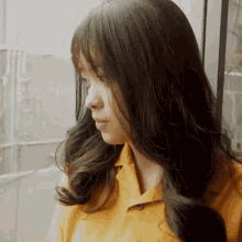 a woman in a yellow shirt is looking out of a window