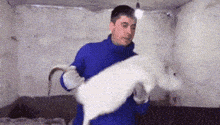 a man in a blue jacket is holding a white rabbit in his arms .