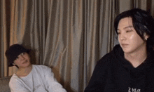 two young men are sitting next to each other in front of curtains .