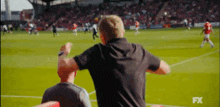 a man in a black shirt is watching a soccer game on a tv screen .