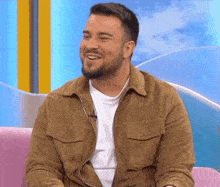 a man with a beard is sitting on a pink couch smiling
