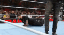 a wrestler is laying on the ground in a wrestling ring while a referee watches .