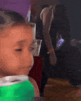 a little girl in a green shirt is looking at the camera .