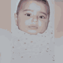 a close up of a baby 's face with a pink flower in the background