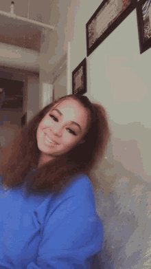 a woman in a blue sweatshirt is smiling in front of a wall with a picture on it that says " i love you "