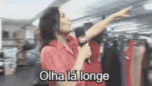 a woman in a red shirt is holding a microphone and pointing at something .