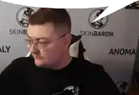 a man wearing glasses is sitting in front of a skinbaron banner