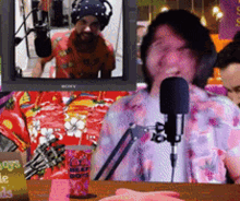a man in a floral shirt is speaking into a microphone in front of a sony monitor