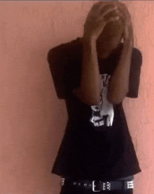 a man is covering his face with his hands while wearing a black shirt and black belt .