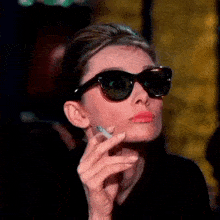 a woman is smoking a cigarette while wearing sunglasses .
